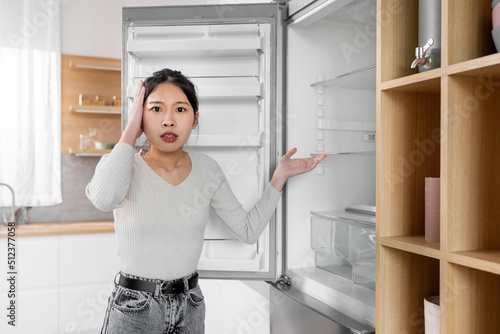 Shocked young korean lady standing by open empty fridge