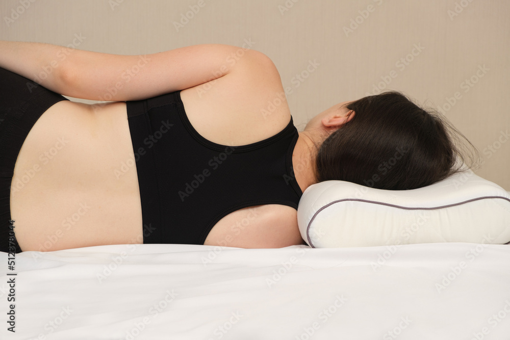 A woman lies on an orthopedic pillow, view from behind. Correct posture and position of the spine during sleep on the side. - obrazy, fototapety, plakaty 