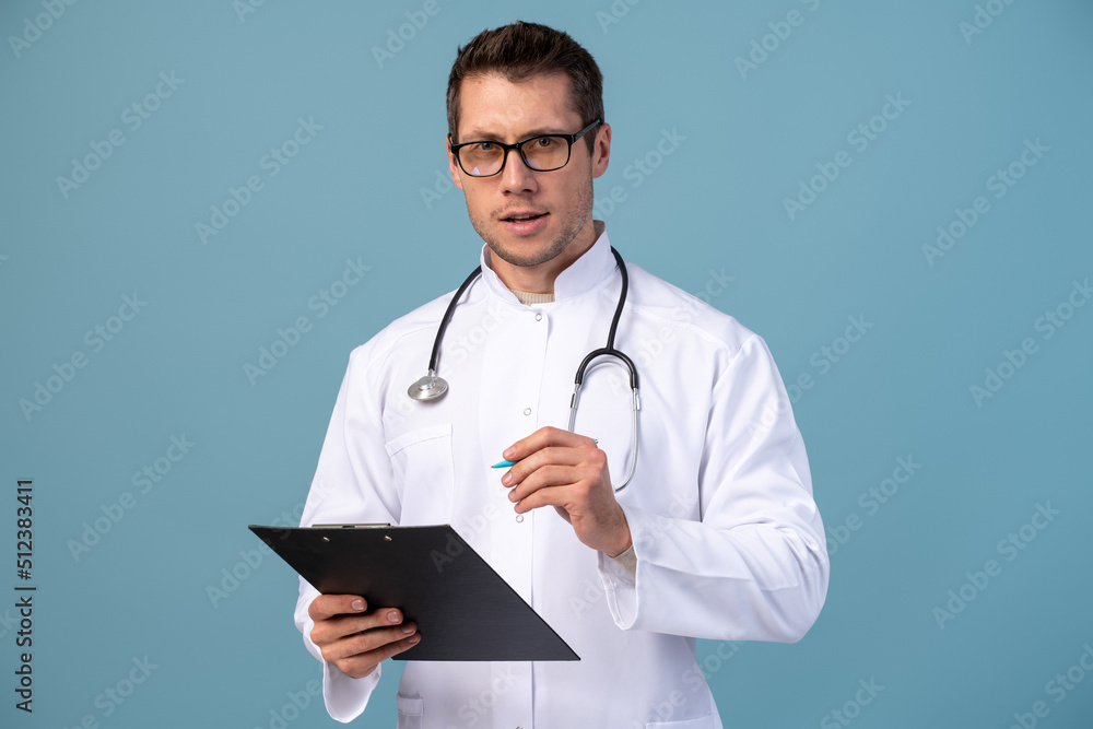 Smiling experienced handsome young doctor man isolated on blue background. Male doctor in medical uniform, stethoscope health card on notepad folder. Healthcare personnel, health, medicine concept Smiling experienced handsome young doctor man isolated on blue background. Male doctor in medical uniform, stethoscope health card on notepad folder. Healthcare personnel, health, medicine concept