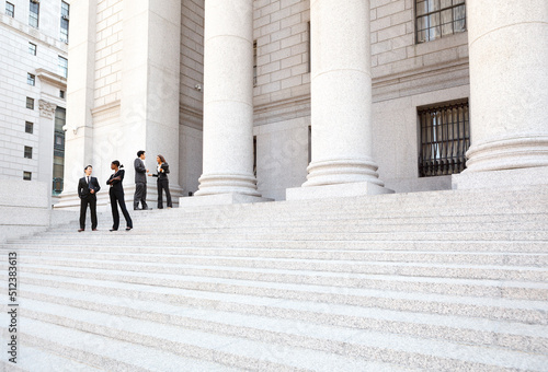 Four people in discussion on the exterior steps of a courthouse. Could be lawyers, business people etc.