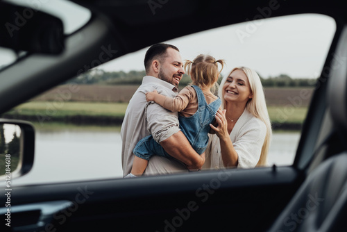 View Through Window Inside of Car, Happy Young Family with Kid Hugging Together and Enjoying Weekend Outside the City