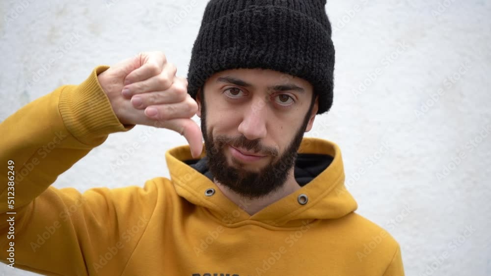 Thumbs Down Signal Shown By A Man In Bonnet Hat And Yellow Clothing. Close-up Thumbs Down Signal Shown By A Man In Bonnet Hat And Yellow Clothing. Close-up
