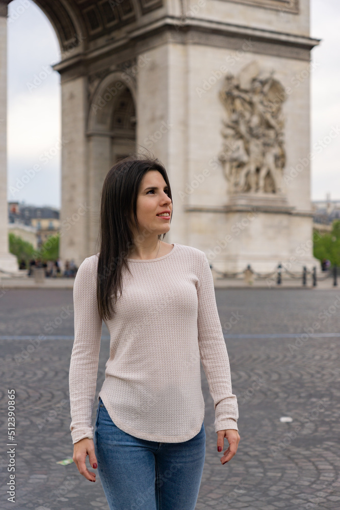 Fototapeta premium Young woman tourist smiling and happy while posing and behind the Triumphal Arch in paris