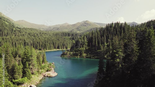 Cinematic drone aerial rising over a beautiful alpine mountain lake surrounded by woods and mountain peaks. Clear blue water on a sunny summer evening. Obernberger lake in Austria. Shot in 6K. photo