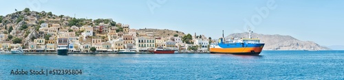Fototapeta Naklejka Na Ścianę i Meble -  Multi-colored houses scattered on hills of Symi island view from water. Coastal town on turquoise sea shore in Greece. Tourist liners moor by seafront