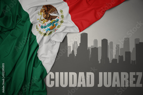 abstract silhouette of the city with text Ciudad Juarez near waving colorful national flag of mexico on a gray background. photo