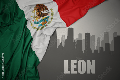 abstract silhouette of the city with text Leon near waving colorful national flag of mexico on a gray background.