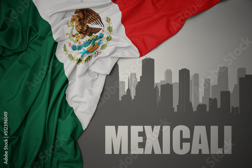 abstract silhouette of the city with text Mexicali near waving colorful national flag of mexico on a gray background. photo