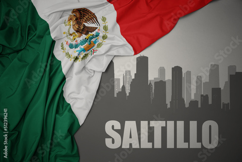 abstract silhouette of the city with text Saltillo near waving colorful national flag of mexico on a gray background.