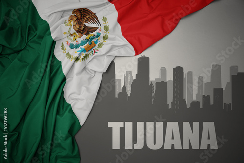 abstract silhouette of the city with text Tijuana near waving colorful national flag of mexico on a gray background. photo