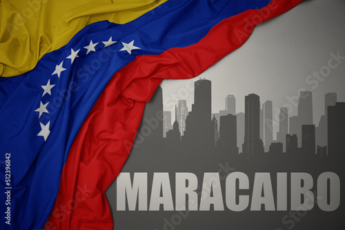 abstract silhouette of the city with text Maracaibo near waving colorful national flag of venezuela on a gray background. photo