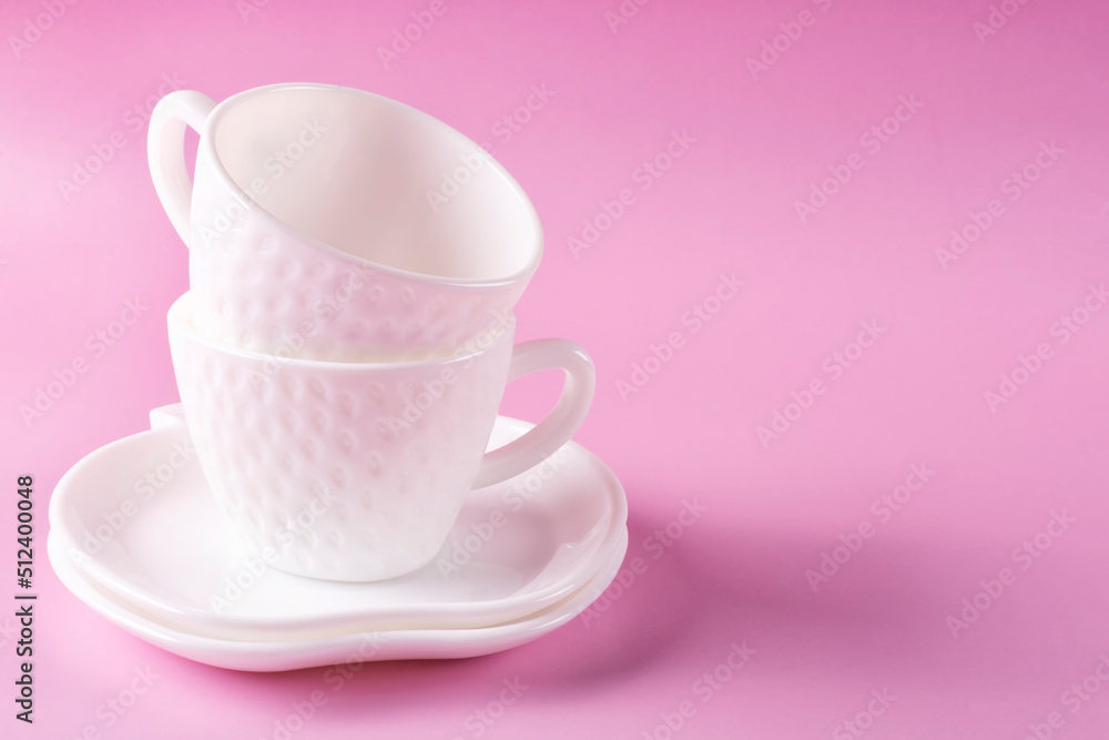 Two beautiful white cups (mugs) in the shape of strawberries and two saucers stacked on top of each other on a pink background. Empty clean dishes. Space for text.