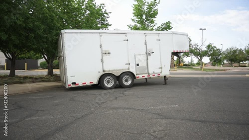 Small white gooseneck cargo trailer in an empty parking lot, static photo