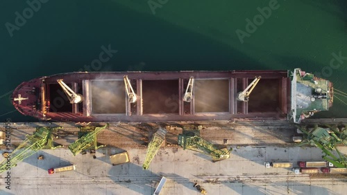 Aerial view of big cargo ship bulk carrier is loaded with grain of wheat in port at sunset