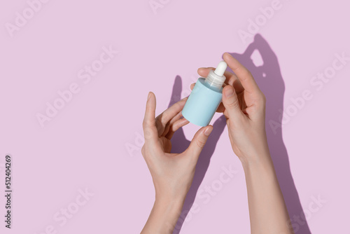 Woman's hands holding blue bottle of cosmetic serum on pink background © LeviaUA