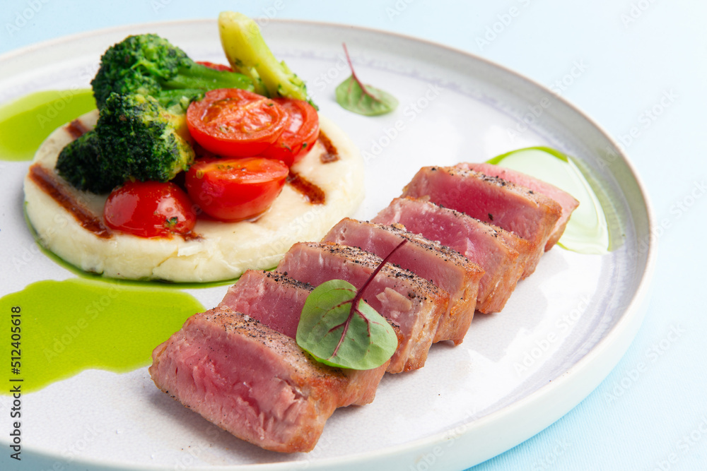 Fried tuna and vegetables in a plate on a blue background.