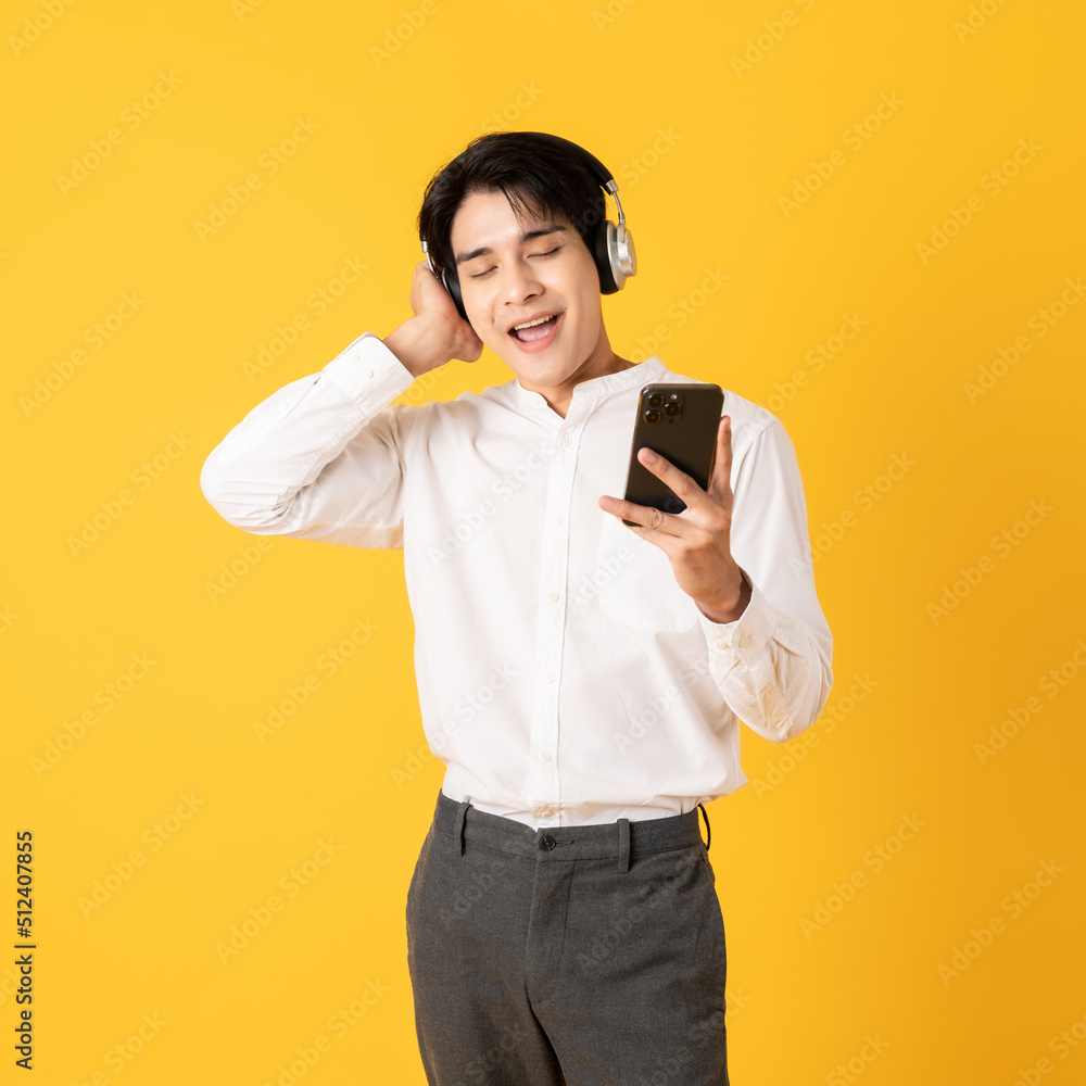 Young good looking asian man using smartphone and headphone listen to music isolated on yellow background Young good looking asian man using smartphone and headphone listen to music isolated on yellow background