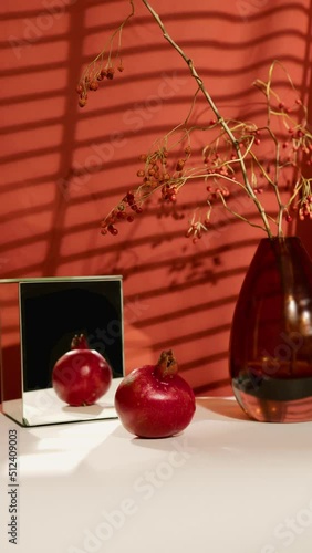 Still life with grapefruit, mirror cube, vase with dried flowers, red cloth with the sun from the window on the background