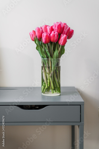 A large bouquet of pink tulips in a transparent vase stands on a blue table. A beautiful bouquet for a girl or for a holiday. Springtime abundance of flowers. Freshness and purity.