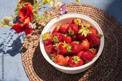 Ripe red strawberries in a white bowl on a table in the garden. Picked strawberries close up.