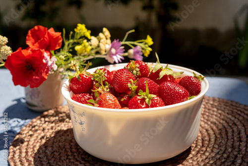 Ripe red strawberries in a white bowl on a table in the garden. Picked strawberries close up.