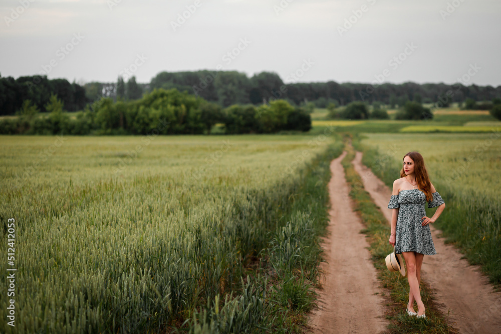 Vinnytsia, Ukraine. May 25, 2022. A girl in a green dress stands in a wheat field and looks at the sky