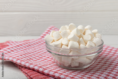 Marshmallow in a glass bowl on a white textured background with a rustic napkin.Closeup gummies.Snacks and snacks for parties.Spice for coffee and cocoa.Winter food concept.Place for text.