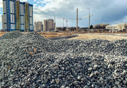 construction of a new microdistrict in the city center. tall, high-rise buildings made of concrete and glass next to a pile of stones. gray stones lie for the construction of the road