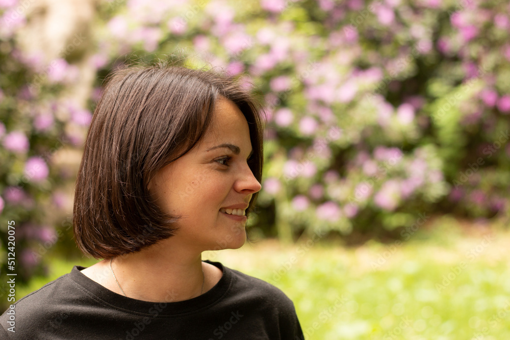 Profile portrait of a beautiful smiling woman in a black T-shirt against the background of a flowering bush Profile portrait of a beautiful smiling woman in a black T-shirt against the background of a flowering bush