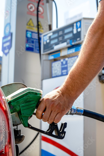 Man pumping gasoline fuel in a car at a self-service gas station. Hand holding a pistol or nozzle pump refueling the car tank.
