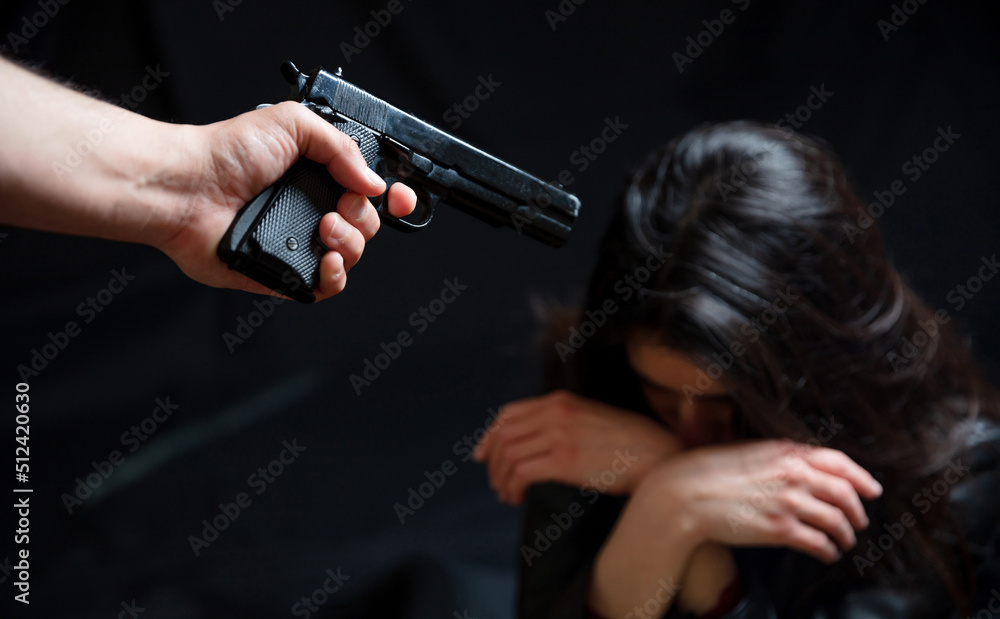 Threatened woman concept. Killer armed with a pistol terrorizes girl who keeps her head bent over. Threatened woman concept. Killer armed with a pistol terrorizes girl who keeps her head bent over.