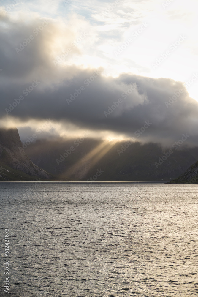Dramatic sky over the mountains of Lofoten Islands, Norway with rays of sunlight pointing through heavy onto the calm ocean. Peaceful, majestic scene of nature. Dramatic sky over the mountains of Lofoten Islands, Norway with rays of sunlight pointing through heavy onto the calm ocean. Peaceful, majestic scene of nature.
