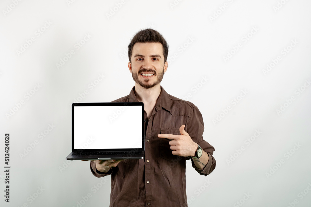 Young man smiling confident wearing casual clothes posing isolated over white background pointing with index finger to laptop pc computer with blank empty screen Young man smiling confident wearing casual clothes posing isolated over white background pointing with index finger to laptop pc computer with blank empty screen