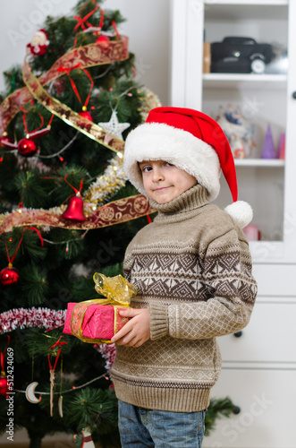 Cute boy in Santa's hat with gift posing near Christmas tree