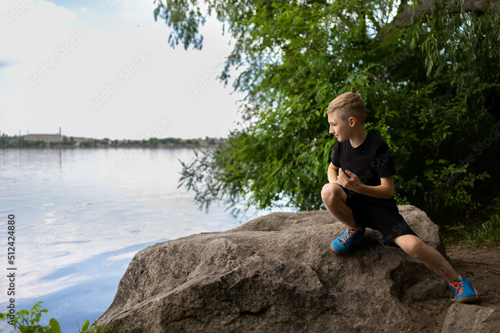 a boy looks into the river sitting on a stone