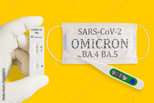 Rapid antigen test kit with positive result during swab COVID 19 testing. Face masks, thermometer and pills isolated on a yellow background. Omicron BA.4 BA.5 variants