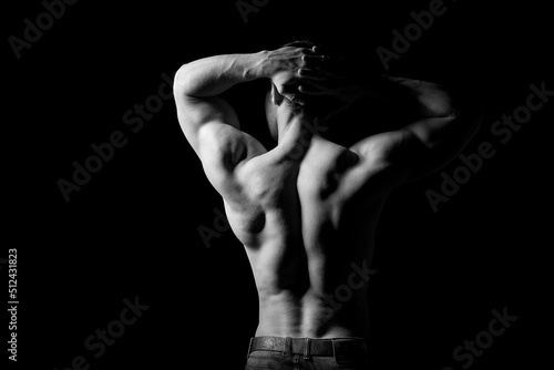 Strong muscular man holding his hands behind his head. Perfect shoulders and back muscles. Dramatic light