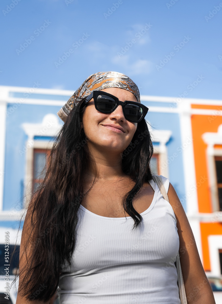 hispanic woman with glasses and headscarf smiles in front of colorful houses