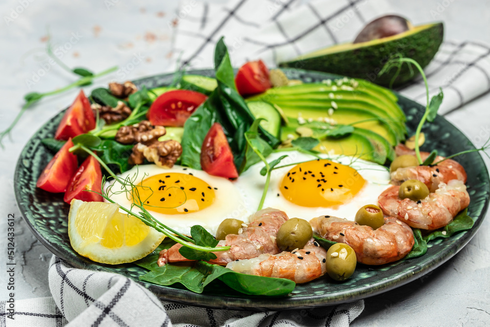 Ketogenic diet breakfast shrimps, prawns, soft fried egg, fresh salad, tomatoes, cucumbers and avocado on a dark background. Keto, paleo lunch. Top view