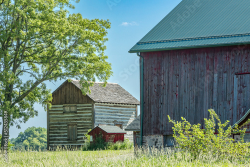 An historic two-story reconstructed log cabin and a vintage wooden dairy barn with a new metal roof in a park.