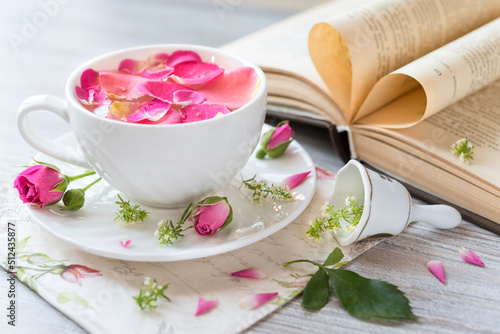 Cup and saucer with tea rose petals with buds, bell and open book. Post card. Romantic mood