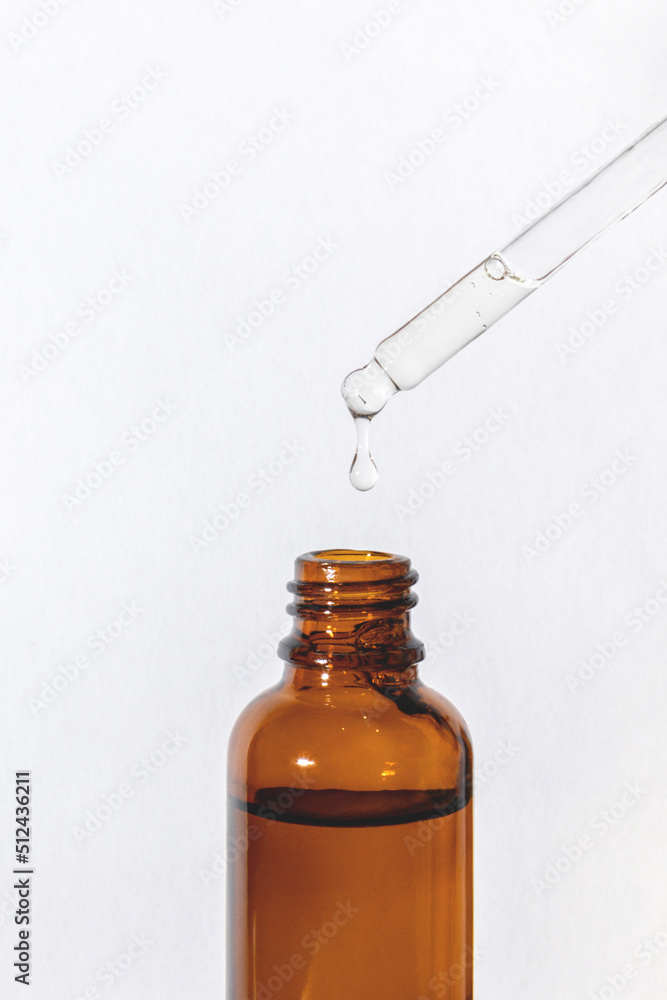 Dripping serum from a pipette with a vial on the side into a glass brown bottle on a white background, vertical close-up Dripping serum from a pipette with a vial on the side into a glass brown bottle on a white background, vertical close-up