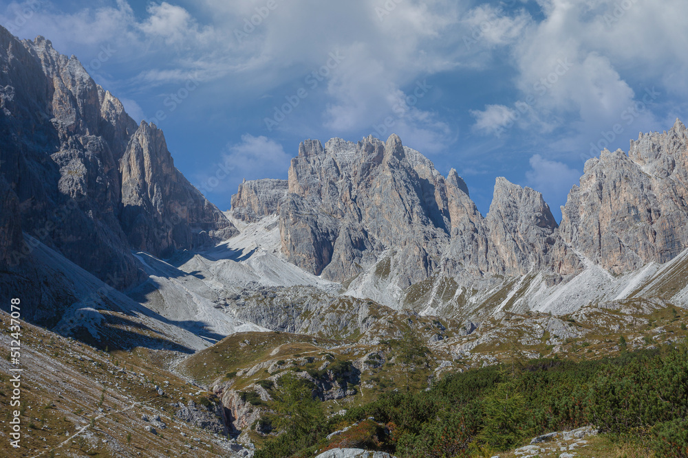 Panorama of rocky ridges of Croda Rossa di Sesto Mountain and Sentinella Pass in Comelico region with green meadows, paths and blue sky, Dolomites, Italy