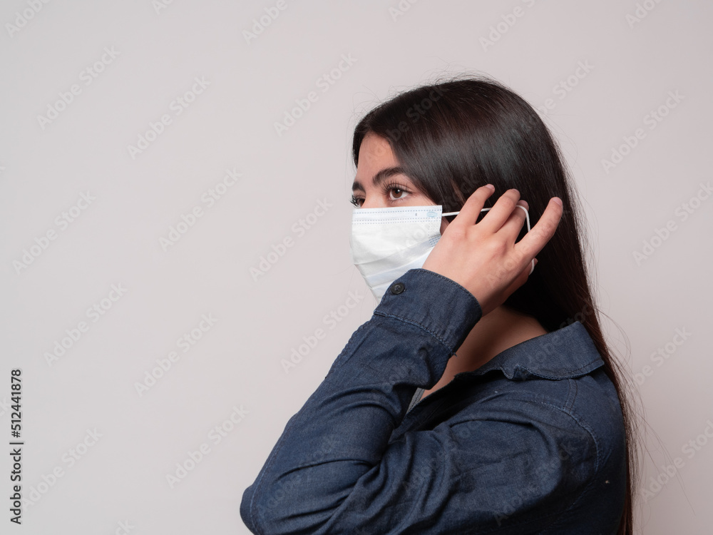close-up of a portrait of a black-haired latina girl putting on a surgical mask, isolated on white background