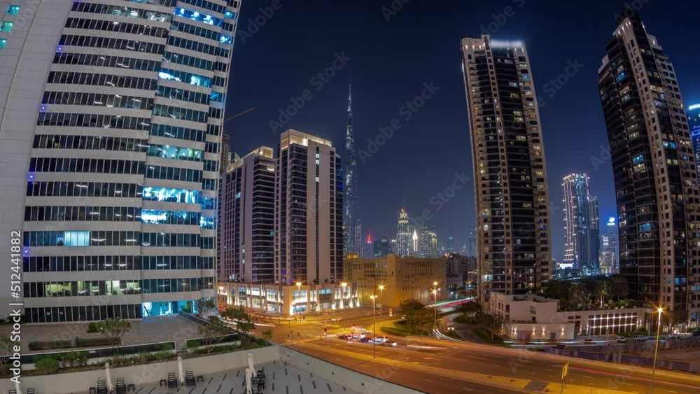 Aerial panorama of Dubai downtown and difc skyscrapers with busy traffic on intersection in Business bay district night timelapse. Chairs near illuminated swimming pool Aerial panorama of Dubai downtown and difc skyscrapers with busy traffic on intersection in Business bay district night timelapse. Chairs near illuminated swimming pool