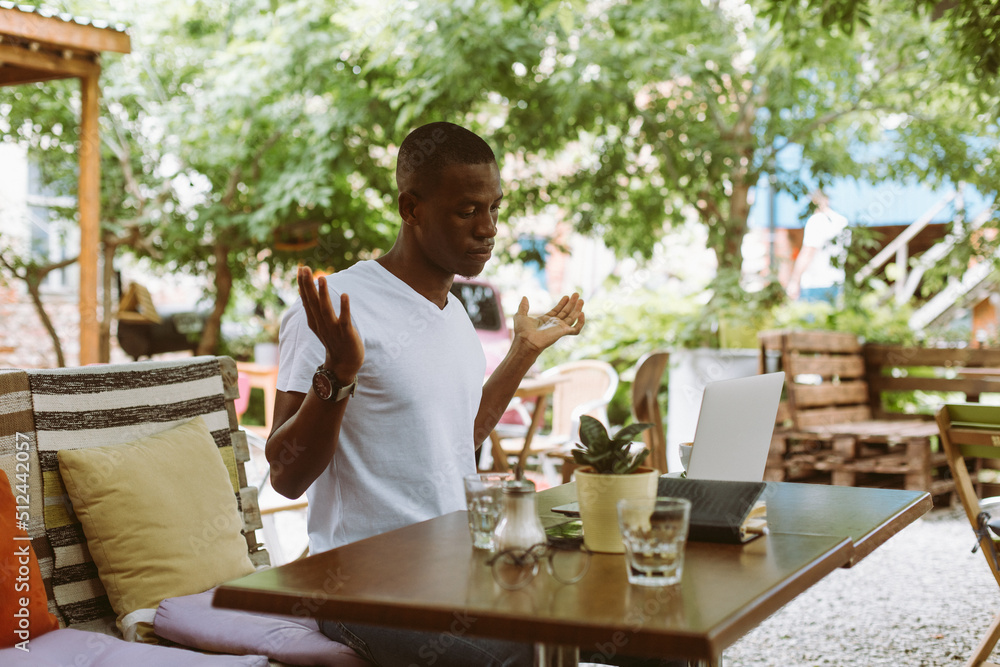Surprised and confused african afro american man with laptop in cafe dont know what to do, throwing hands in outdoor cafe. Business and freelancing problems. Waiting results of online web meeting Surprised and confused african afro american man with laptop in cafe dont know what to do, throwing hands in outdoor cafe. Business and freelancing problems. Waiting results of online web meeting
