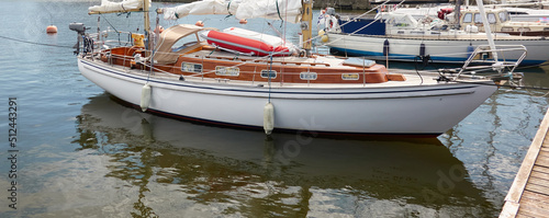 An elegant two masted sailboat (ketch) moored to a pier in a yacht marina. Wooden teak deck, rigging equipment, mast winch, ropes. Transportation, cruise, vacations, service and repair themes photo