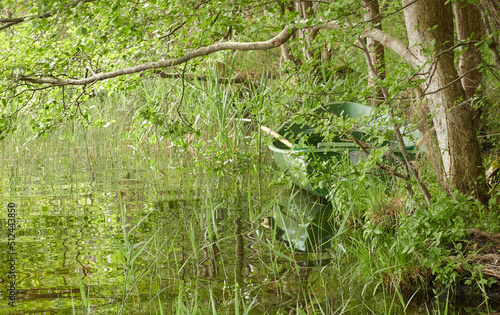 Small green boat anchored in forest lake. Scandinavia. Transportation, traditional craft, recreation, leisure activity, healthy lifestyle, local tourism, sport, rowing, hiking, summer vacations themes photo