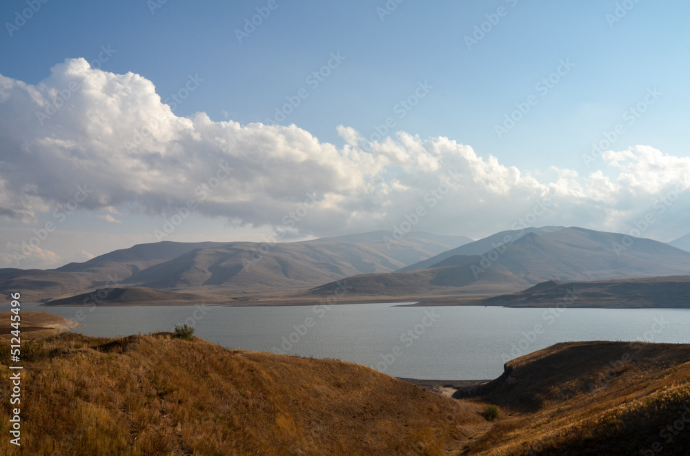 The rays of the sun are reflected in the water of a picturesque reservoir surrounded by mountains. Natural landscapes of Armenia