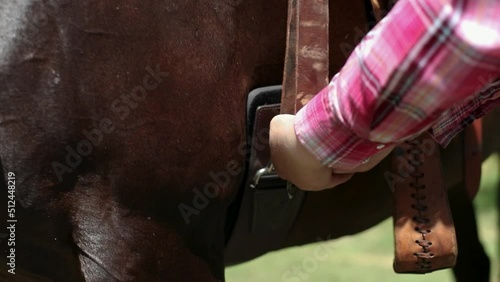 Hands tightening a cinch on a western saddle. 